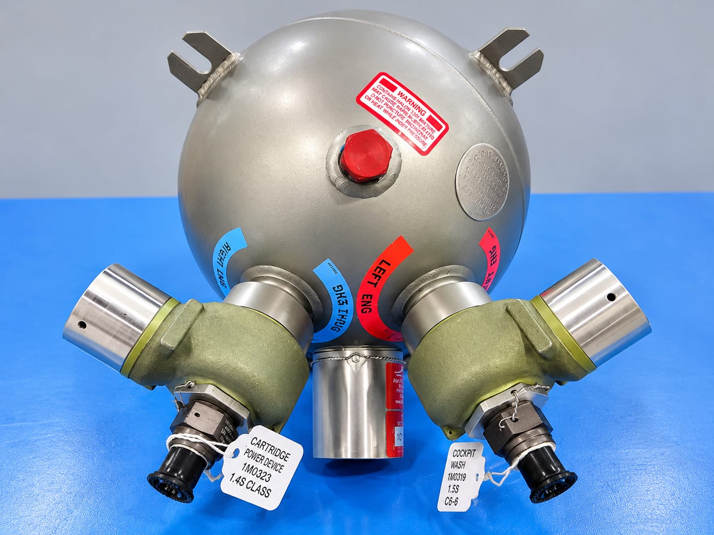 Aircraft fire extinguisher bottle with tagged discharge heads on a blue workbench
